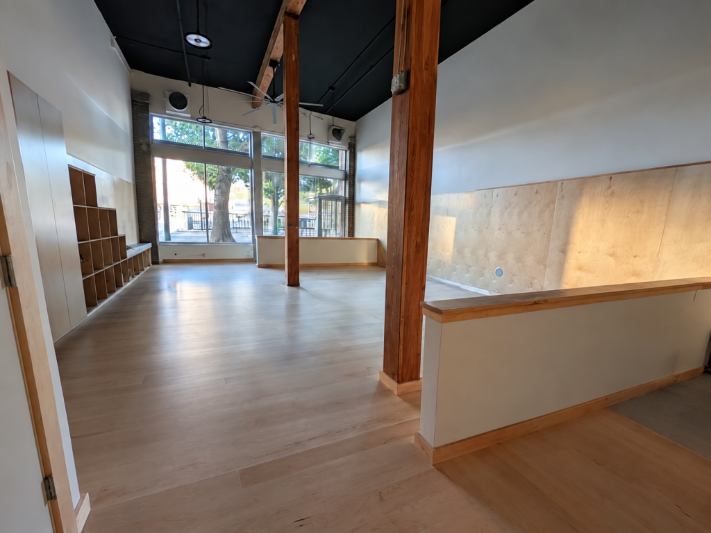 Second view of the Seattle Capoeira Center showing the sprung maple wood floor, tall ceilings, wood columns, and open training space.